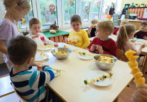 Dzieci samodzielnie przygotowują i trzymają kolorowe szaszłyki owocowe.
