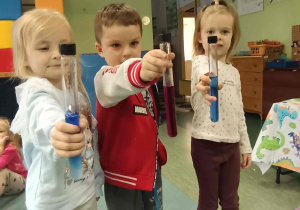 Dzieci biorące udział w przedszkolnych warsztatach chemicznych z probówkami zawierającymi kolorowe płyny.