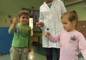 Dzieci trzymają probówki w obecności osoby prowadzącej warsztaty.