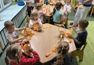 Dzieci owijają bibułą rączkę koszyczka.