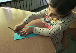 Dziewczynka odrysowuje swoją dłoń na niebieskiej kartce papieru.
