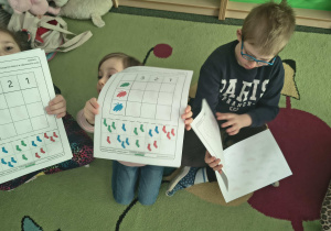 Dzieci pokazują zadanie do wykonania w kartach pracy.